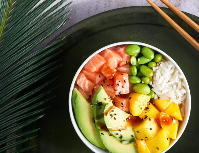 Salmon Poke bowl Raw fish salad Asian trendy food, mango, soy beans edamame, rice, avocado, served in bowl on tropical leaves. Marble table, top view. Copyspace. nutrition concept, fast healthy lunch.