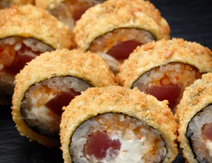 Hot fried sushi roll with salmon. Sushi menu. Japanese food. Hot fried sushi roll on black background Hot fried sushi roll with salmon. Sushi menu. Japanese food. Hot fried sushi roll on black background.